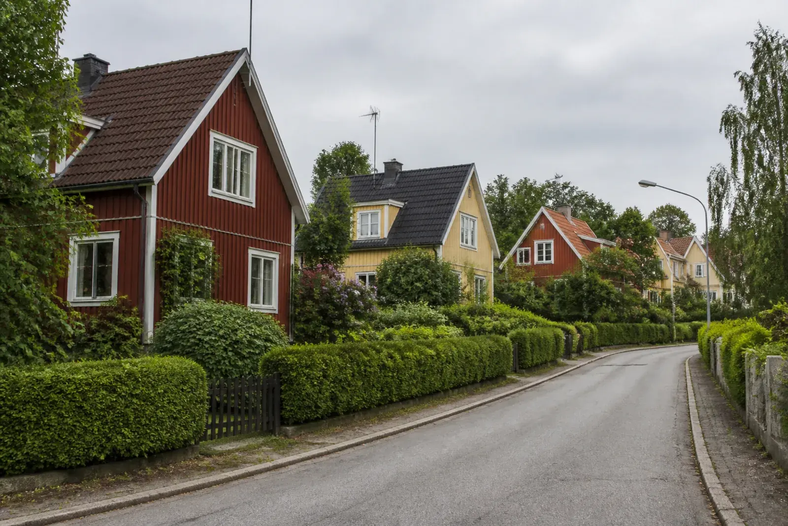 Villagata med trähus i falurött och ljusgult bakom klippta häckar, typiskt för äldre villakvarter i Södertälje