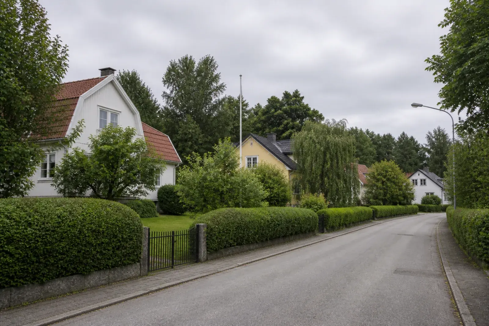 Villor indragna bakom höga häckar längs en bred, lugn gata, typiskt för villaområden med större tomter
